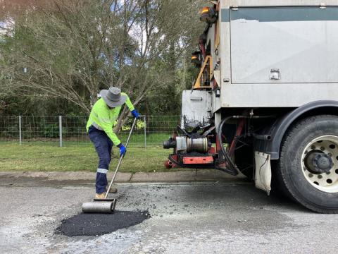 Pothole filling at Jilliby road worker filling pot hole and using roller to flatten