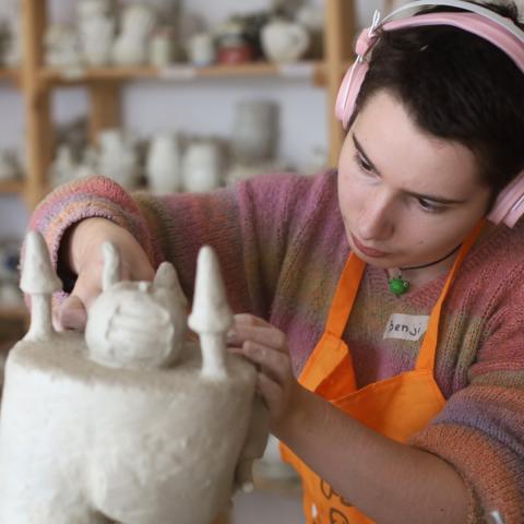 young woman in ceramic studio working on art with headphones on