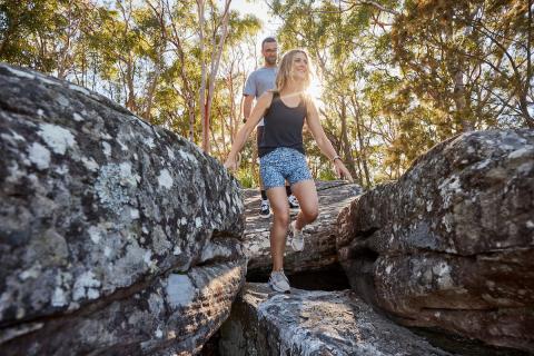 woman walking in the bush between bush rock boulders with man behind