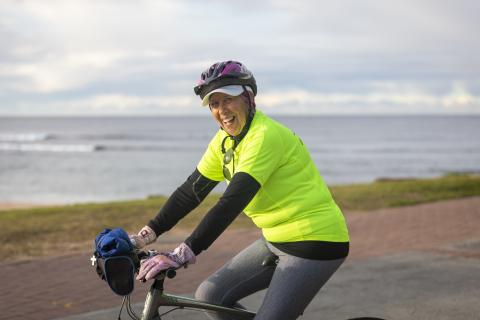 Open Space Strategy image of older lady Older lady riding a bike near the beach