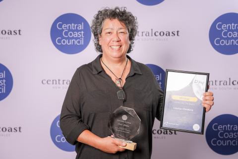Australia Day Award 2025 award winner, Louise Chiekrie (Community Life Award) Woman in balck top holding award Mayor in front of screen with Council logo