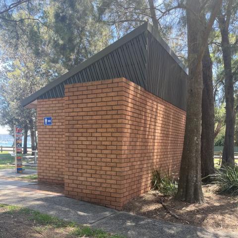 Jirramba Reserve old facility Old brown bricked toilet building with slanted roof. Water in background. Trees surrounding.