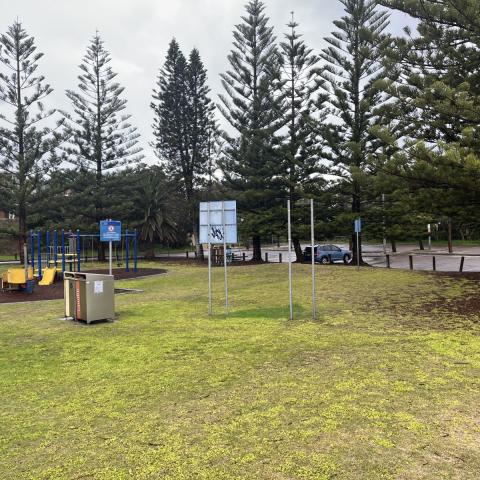 Site of new facility building at Karagi Point Reserve Photo of Karagi Point Reserve with grass, pine trees, playspace, bins, signage and carpark